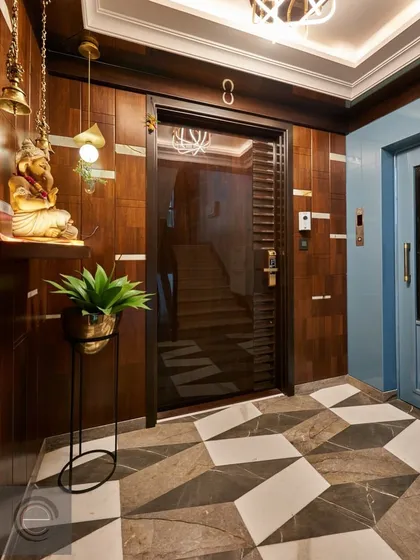 This entrance features warm wood paneling, a geometric-tiled floor, and traditional Indian decor elements like hanging temple bells, creating a welcoming and culturally rich entryway.