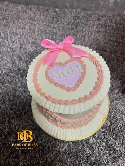 Another angle of the tiered "Mom" cake with delicate piping and a pink ribbon.