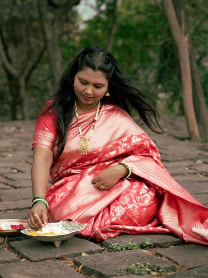 The bride-to-be, dressed in a stunning red saree, prepares for a traditional ritual. The soft, natural light and her graceful posture create a timeless and elegant portrait.