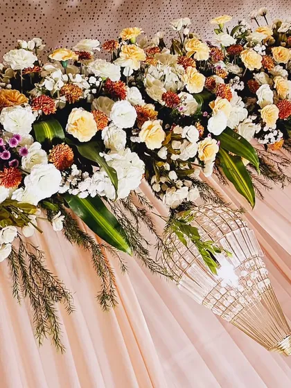 A close-up of a floral runner, featuring a beautiful mix of white, peach, and yellow roses with hints of marigold. The hanging lantern adds a touch of elegance to the arrangement.