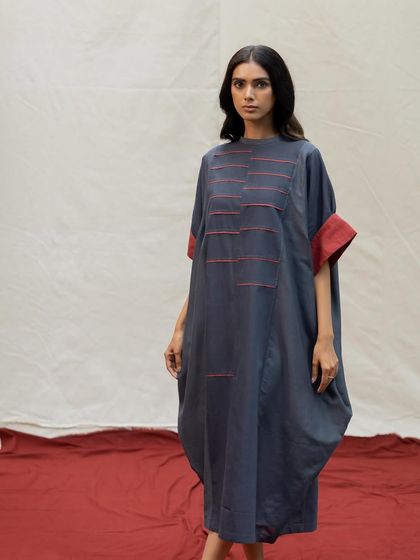 A unique cocoon-shaped dress in a deep charcoal grey, with minimalist red line details for a touch of artistic flair.