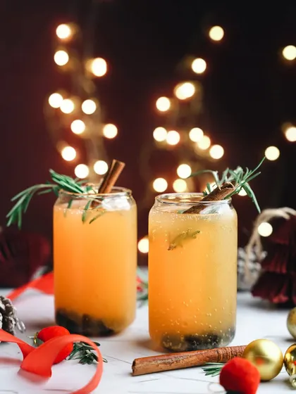 'Tis the season for festive drinks. This shot features a warm, spiced winter drink with cinnamon and rosemary, set against a backdrop of Christmas lights.