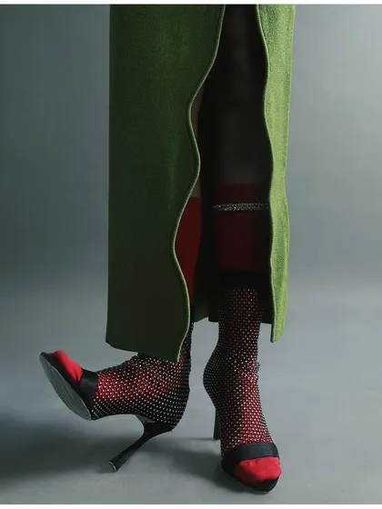 A detail-oriented shot focusing on the lower half of an outfit. The image highlights the layering of fishnet stockings, red socks, and unique heels, showcasing creative styling.