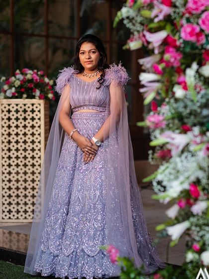 This bride chose a stunning lavender lehenga for her engagement, featuring a modern cut with a flowing cape and feather details on the shoulders. It's a perfect blend of contemporary style and delicate charm.