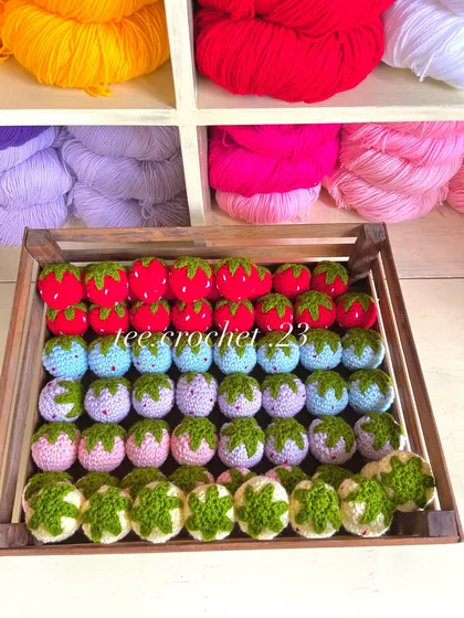 A wooden crate filled with my crochet strawberries and other fruit-themed keychains.