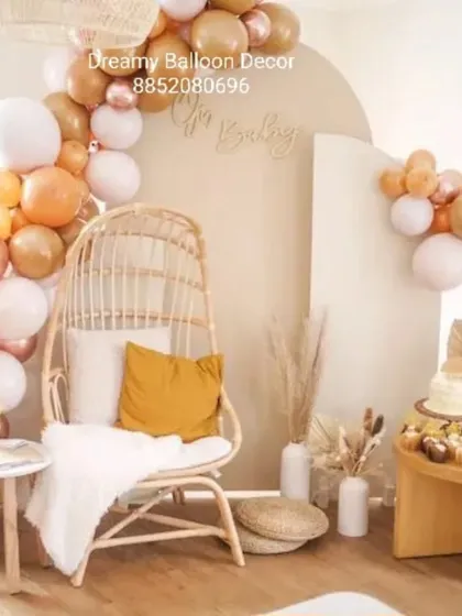 For a modern and minimalist baby shower, I used a boho theme. This setup includes a natural rattan chair, a simple balloon garland in neutral and rose gold tones, and pampas grass for a soft, elegant look.