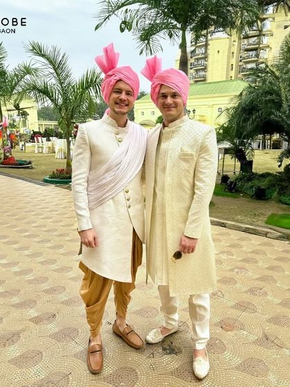 Twinning in style for a day wedding. These gentlemen are wearing our rental sherwanis, one in a classic off-white and the other an Indo-western style with a draped sash, both topped with pink safas.