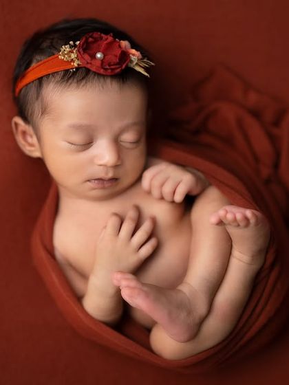 This baby is cozily wrapped in a rust-colored swaddle, showing a classic newborn pose that highlights their tiny features.