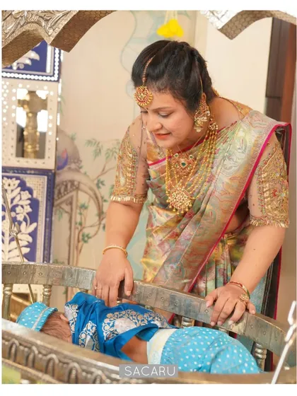 Our client Bhavna at her baby's naming ceremony, wearing a custom blouse with sheer sleeves and intricate cutwork embroidery with French knots.