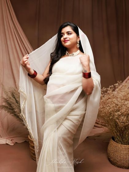 The sheer white fabric of the saree's pallu creates a soft, delicate veil, adding a touch of mystique and elegance to this portrait.