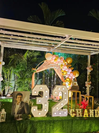 A personalized 32nd birthday celebration at night. The setup features large marquee numbers, a balloon arch, and framed photos of the guest of honor, all under a beautifully lit pergola.
