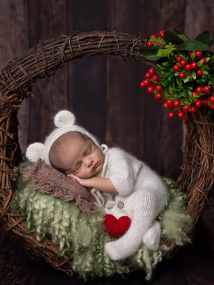 A cozy winter-themed shot with a baby in a white bear onesie, nestled in a wreath with festive red berries. The little red heart adds a pop of color and love.