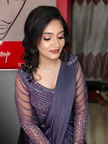 An elegant engagement look featuring soft pink eyeshadow, winged liner, and a matching lip color. The side-parted soft curls add a touch of romance to her embellished lavender saree.