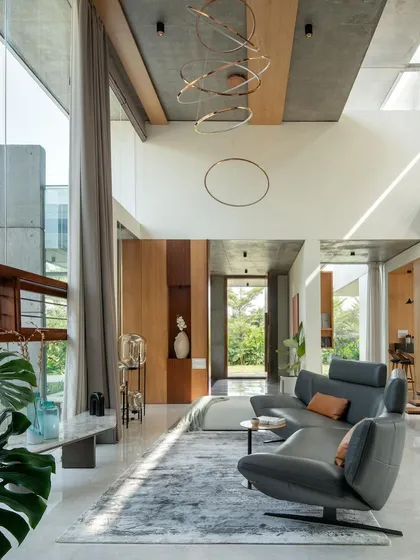 The double-height living area is bathed in natural light from large glass panels and skylights. The space is characterized by an exposed concrete ceiling and a minimalist aesthetic, with views of the garden from every angle.