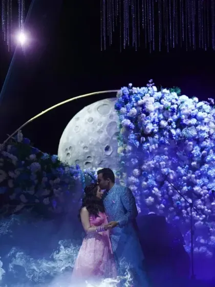 A magical moment as the couple shares a kiss under a stunning floral moon installation, part of our 'Starry Night' engagement theme.
