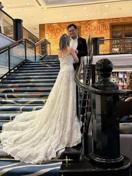Making dreams come true, one outfit at a time. This couple shares a beautiful moment on the stairs, styled in a classic black suit and a white lace wedding gown with a dramatic train.