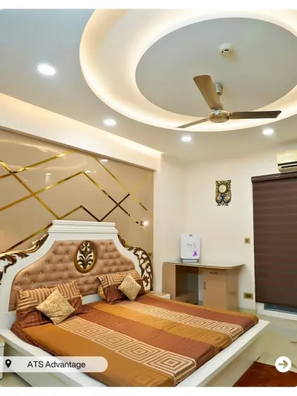 A grand, traditional bedroom with an ornate tufted headboard and a gold-accented wall. The circular false ceiling design adds to the room's opulence.