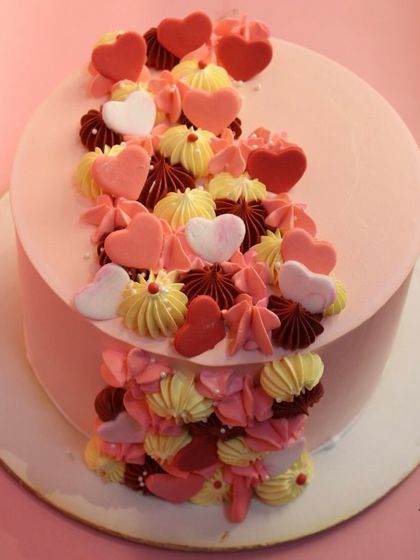 A modern and artistic cake with a cascade of hearts and piped swirls in shades of pink, red, and yellow. A vibrant celebration of love.
