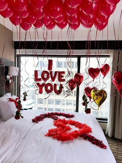 This is our classic romantic room decoration, perfect for proposals and anniversaries. The setup includes a ceiling filled with red balloons, 'I LOVE YOU' foil letters above the bed, and heart-shaped balloons framing the window view.
