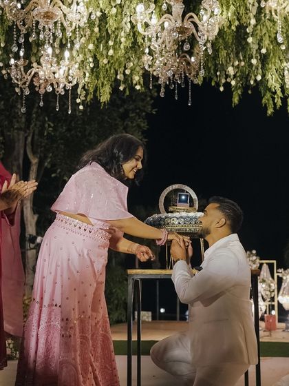 The groom gets down on one knee to propose to his bride during their beautifully decorated engagement party.