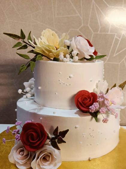 A simple yet beautiful two-tiered cake perfect for an intimate wedding or celebration. It's decorated with handcrafted sugar flowers in red, white, and yellow, creating a classic and romantic look.