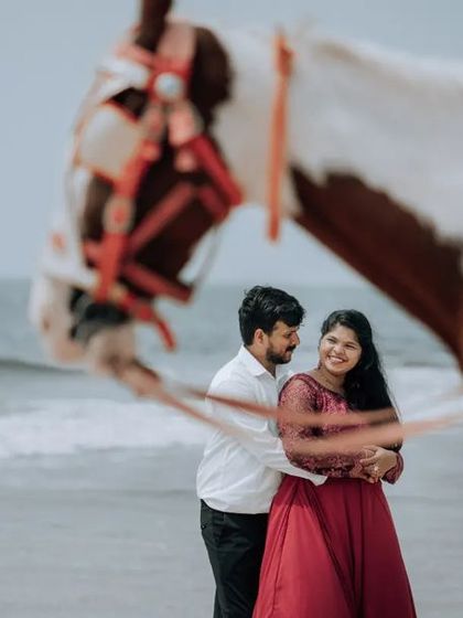 A creative pre-wedding photo on the beach, with the horse's head creating a natural frame for the couple in the background.