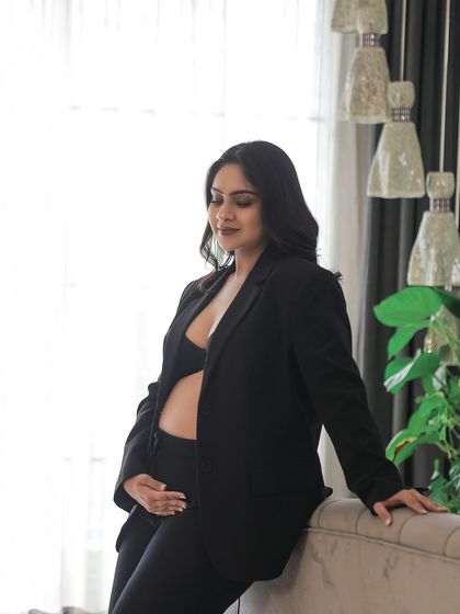A quiet moment of reflection. This portrait, taken in a home-like setting, shows the mother-to-be in a stylish black suit, looking thoughtful and serene.