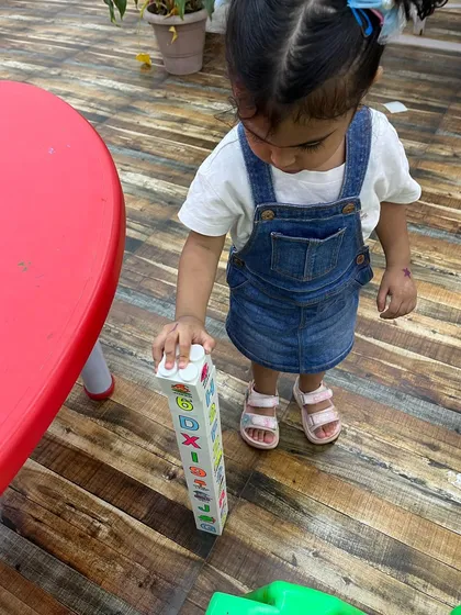 A toddler proudly stands by her alphabet block tower. Play-based learning helps children grasp concepts naturally.