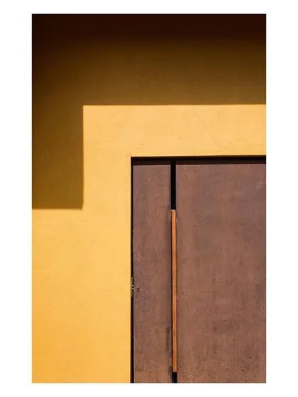 A minimalist composition of a corten steel-clad door against a yellow wall. This detail shot captures the project's bold use of color and material.