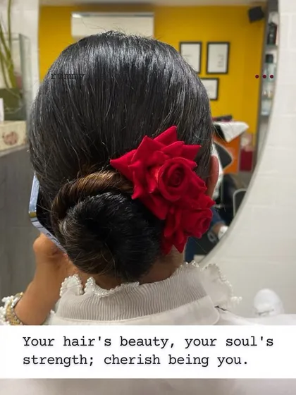 A classic low bun accented with a single, vibrant red rose. This hairstyle is a statement of elegance and is perfect for clients who appreciate timeless beauty.