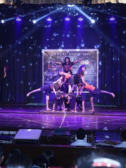 The stage is our playground. Here, students create a dynamic pose with varying levels of elevation and flexibility, showing the diverse skills learned in our gymnastics program.