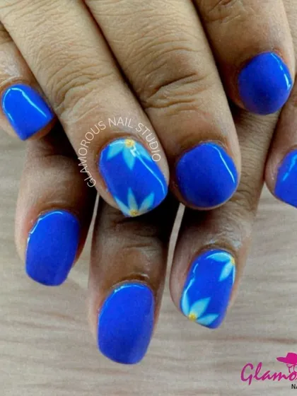 Bold blue nails are softened with the addition of hand-painted white and yellow floral accents, creating a beautiful contrast.