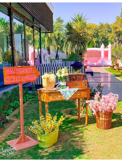 A charming little corner of the 'Secret Garden', with a rustic wooden table, baskets of flowers, and a hand-painted signpost. These small vignettes add depth and detail to the overall experience.