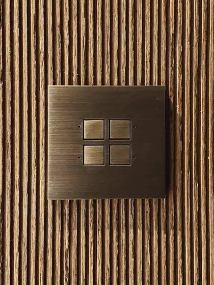 A detail of a brass switch plate set against a fluted wooden panel in the Worli Duplex. The combination of the machined metal and the natural wood grain is a recurring theme in our work.