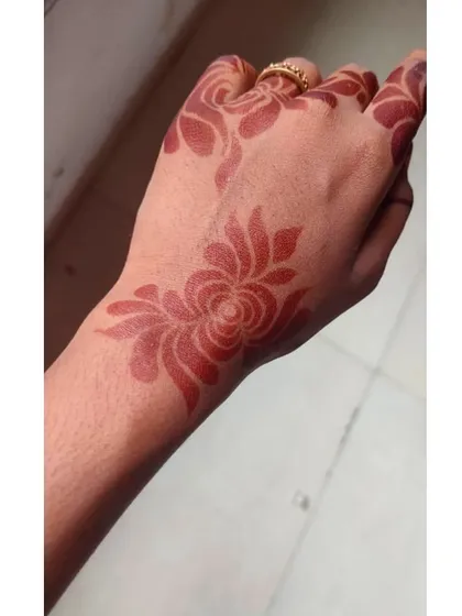 A single, stylized floral motif on the back of the hand. The stain is just starting to develop its beautiful red color.