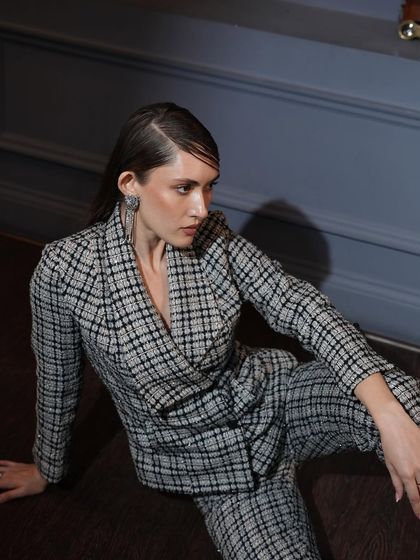 A model seated on the floor in a black and white plaid pantsuit. The wet-look hair and dramatic pose give this classic pattern a high-fashion, edgy update.