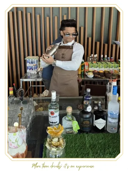 A mixologist shakes a cocktail with style at an outdoor event. The setup, complete with premium spirits like Hendrick's Gin and Grey Goose Vodka, shows our commitment to quality ingredients.