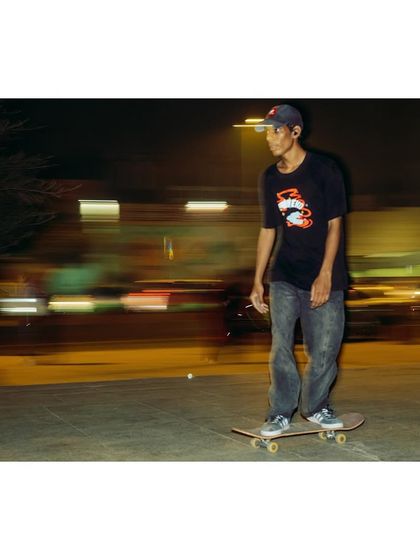 A night shot of a skater at Mandi House, with light trails from the city traffic blurring in the background. The image captures the cool, focused vibe of the late-night skate scene.