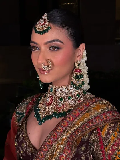 This is the kind of high-quality, professional look you can create with our rental collection. This model is wearing a complete bridal set, including a detailed choker with green and red accents, matching earrings, maang tikka, and nath.