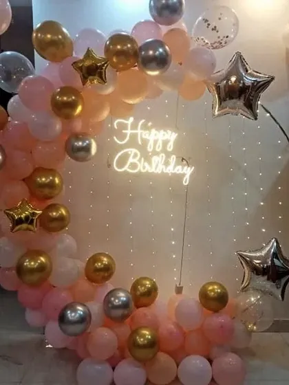 A rose gold, pink, and silver balloon arch with star foil balloons and fairy lights.