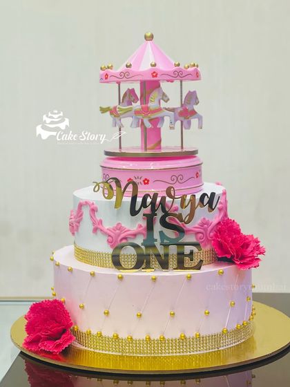 A beautiful carousel-themed cake for a first birthday. This three-tier pink and gold cake is topped with a miniature rotating carousel, adding a touch of whimsy and magic.