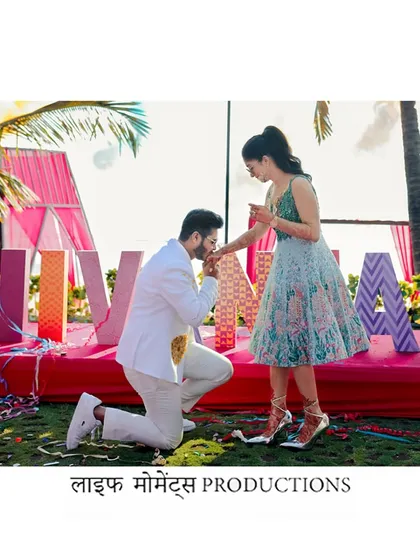 A sweet moment from a wedding carnival in Goa. The groom-to-be proposes to his bride in front of a colorful, festive backdrop.