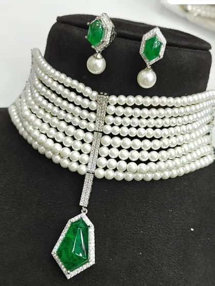 This modern multi-strand pearl choker offers a chic and elegant look. It features a central emerald green stone pendant and comes with matching pearl drop earrings, available for rent in Mumbai.
