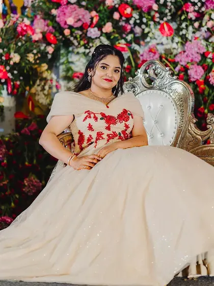 A princess moment. This client is seated on an ornate chair, her voluminous off white ball gown spreading around her. The red floral embroidery on the bodice adds a beautiful pop of color and romance.