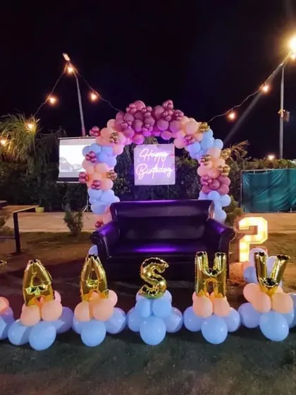 An outdoor birthday party at dusk for Kashvi. The setup includes a balloon arch with a neon sign over a sofa, and the name spelled out with individual balloon letters.