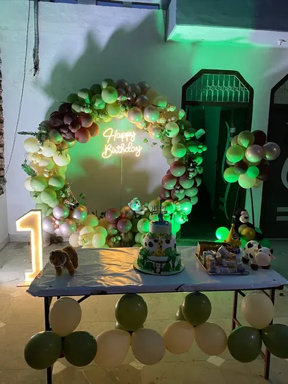 The jungle-themed first birthday setup with the cake table in front. The green lighting adds to the jungle ambiance.