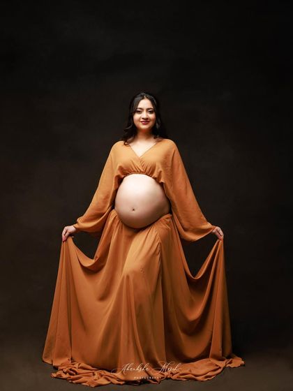 A happy and proud portrait showcasing the bare bump in a beautiful mustard-colored gown with flowing sleeves.