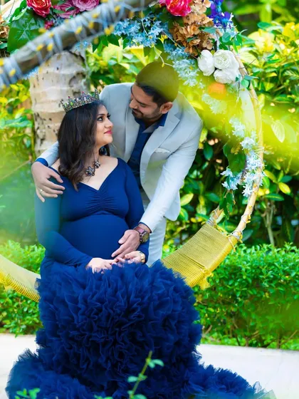 A fairytale moment on a garden swing. This couple shares a loving look, with the mom-to-be in a magnificent blue gown, creating a romantic and whimsical scene.