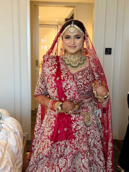 A full view of a traditional Phera look. The bride's makeup is minimal and fresh, allowing her heavily embroidered red lehenga and stunning jewelry to shine.