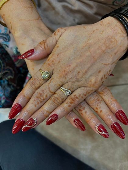 Another view of the classic red nails with rhinestone details. The shaping and application are flawless, showing the quality of training.